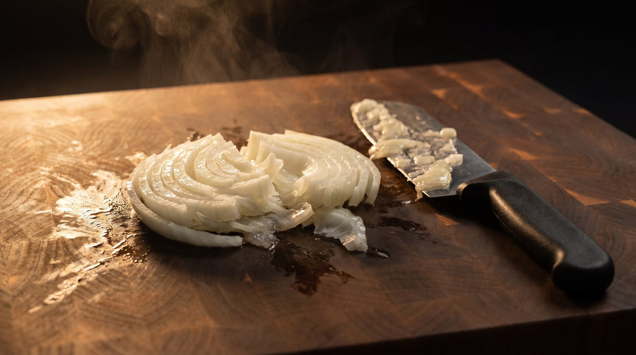 An onion crushed and split apart by a blunt blade, juice on the board